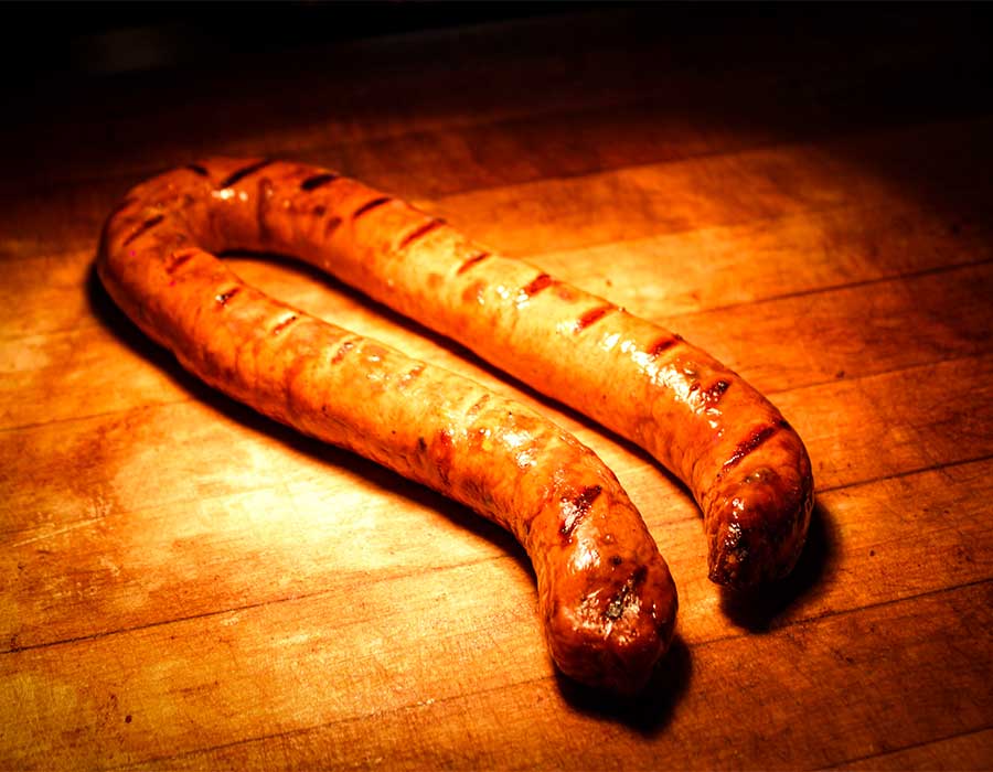 Two grilled sausages from Klinger's Real BBQ Menu on a wooden cutting board under warm lighting.