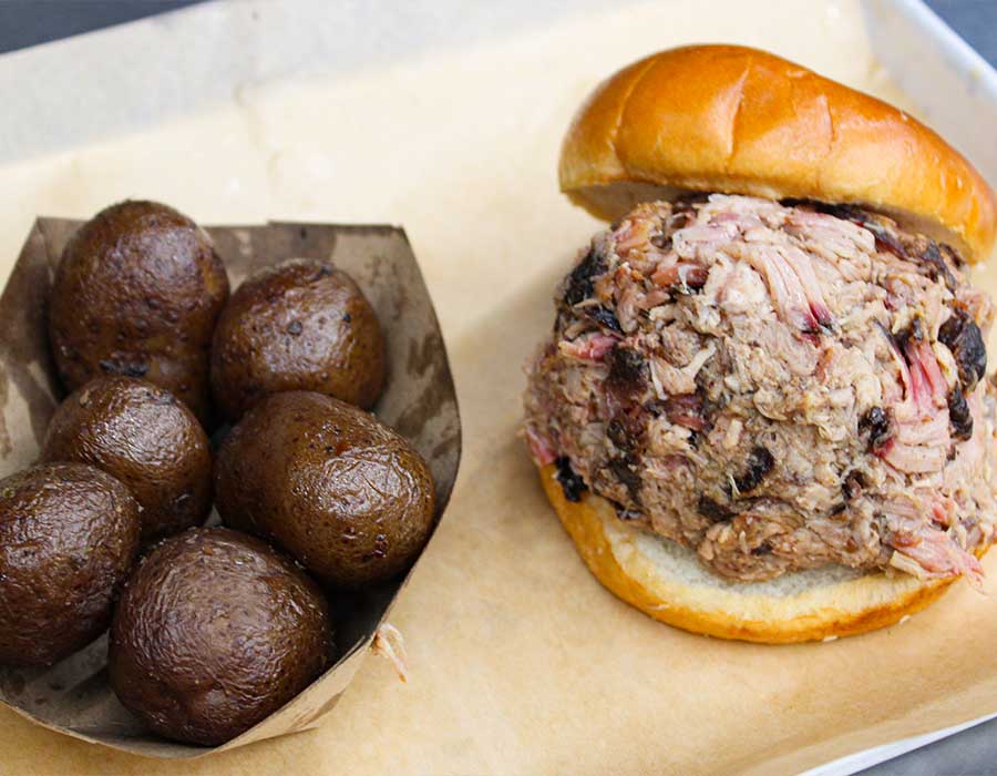 Pulled pork sandwich from Klinger's Real BBQ Menu with glazed mushrooms on parchment paper.